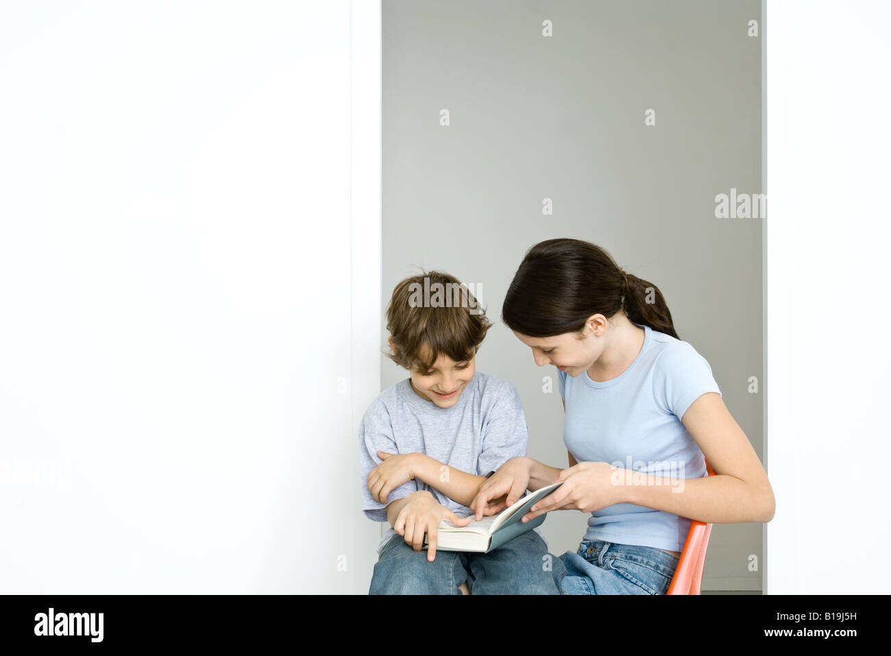 Preteen girl and little brother reading book together Stock Photo