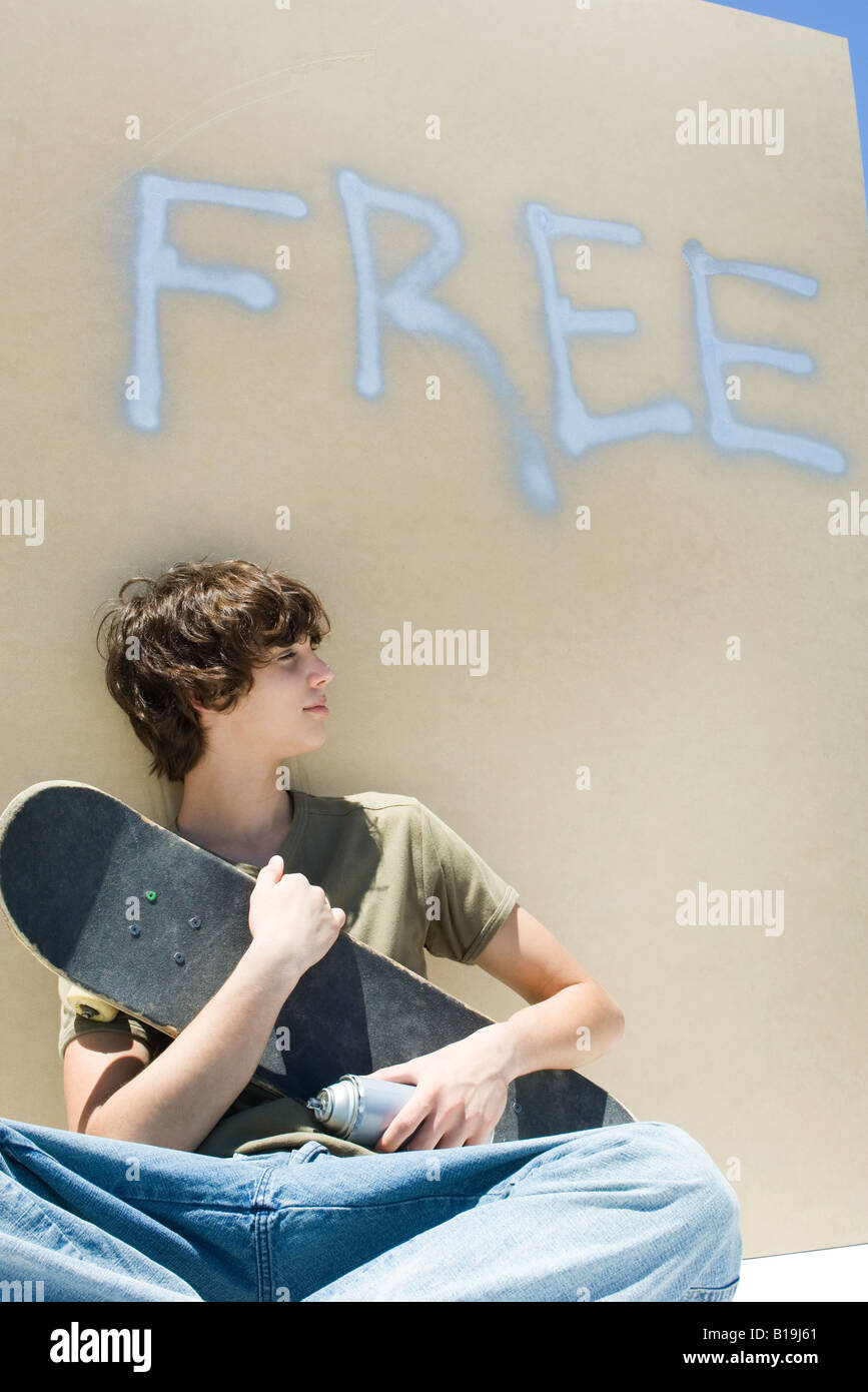 Teen boy holding skateboard and spray paint can, under the word "free" on wall Stock Photo