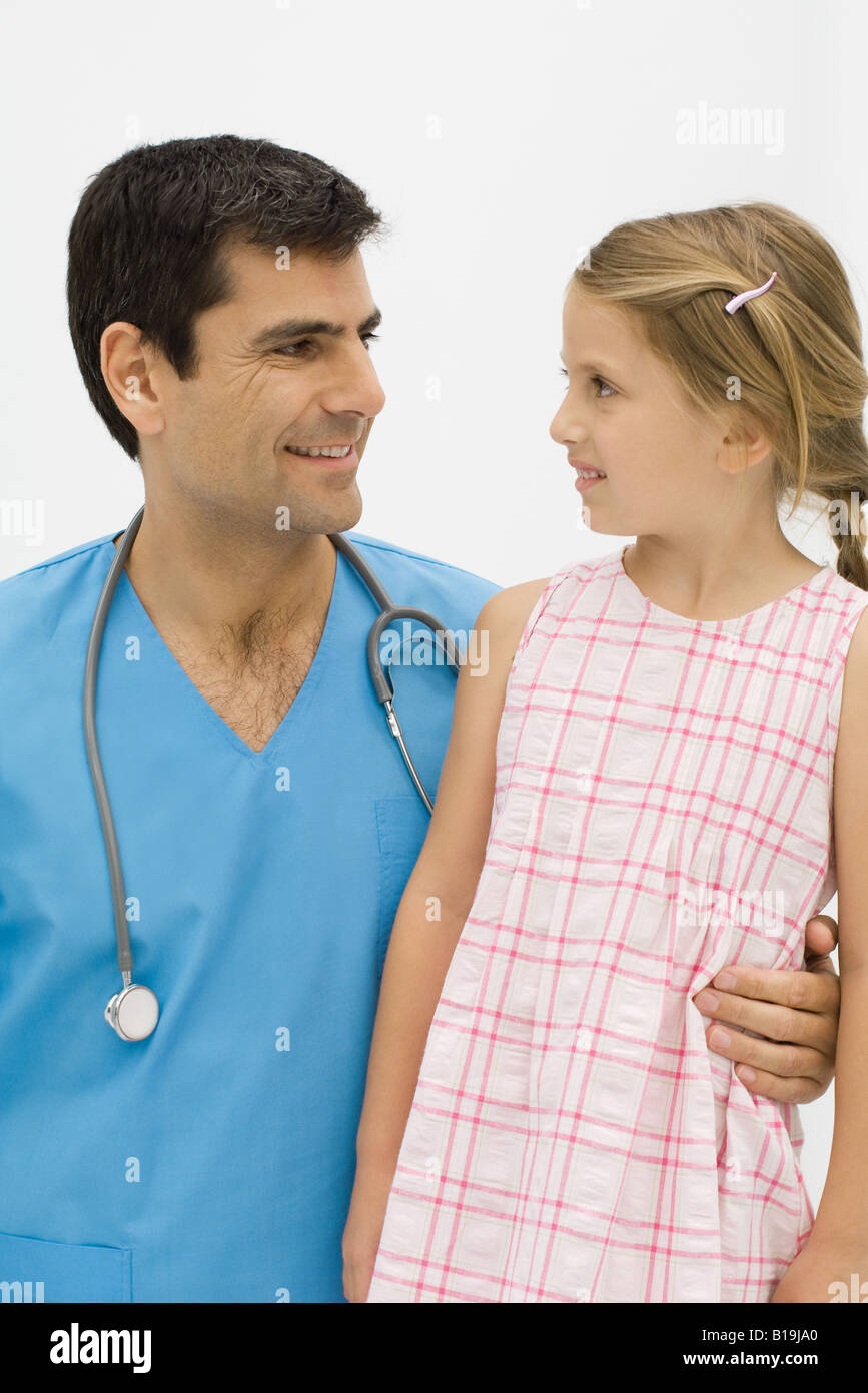 Doctor with arm around little girl's waist, both smiling at one another