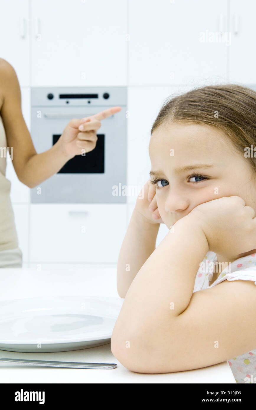 Girl sulking at kitchen table, mother shaking finger, cropped view Stock Photo