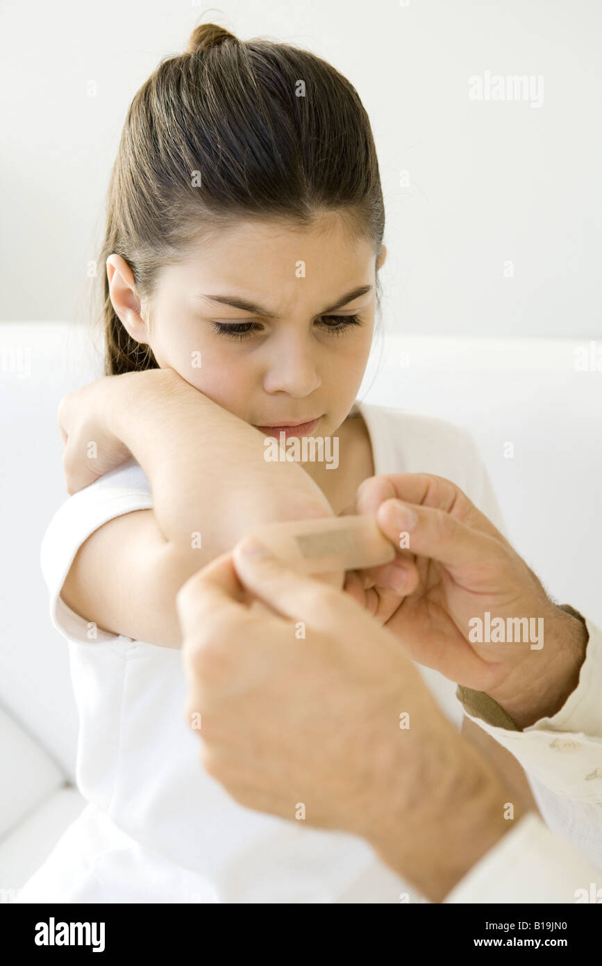 Man putting adhesive bandage on little girl's elbow, cropped view Stock Photo