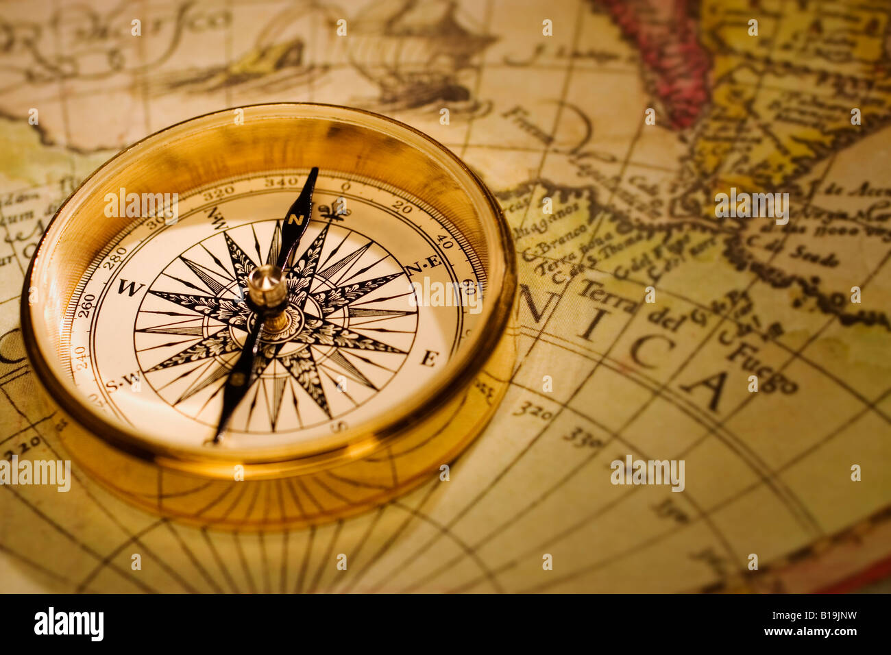 An antique gold compass set upon a sixteenth century map of the world Stock Photo