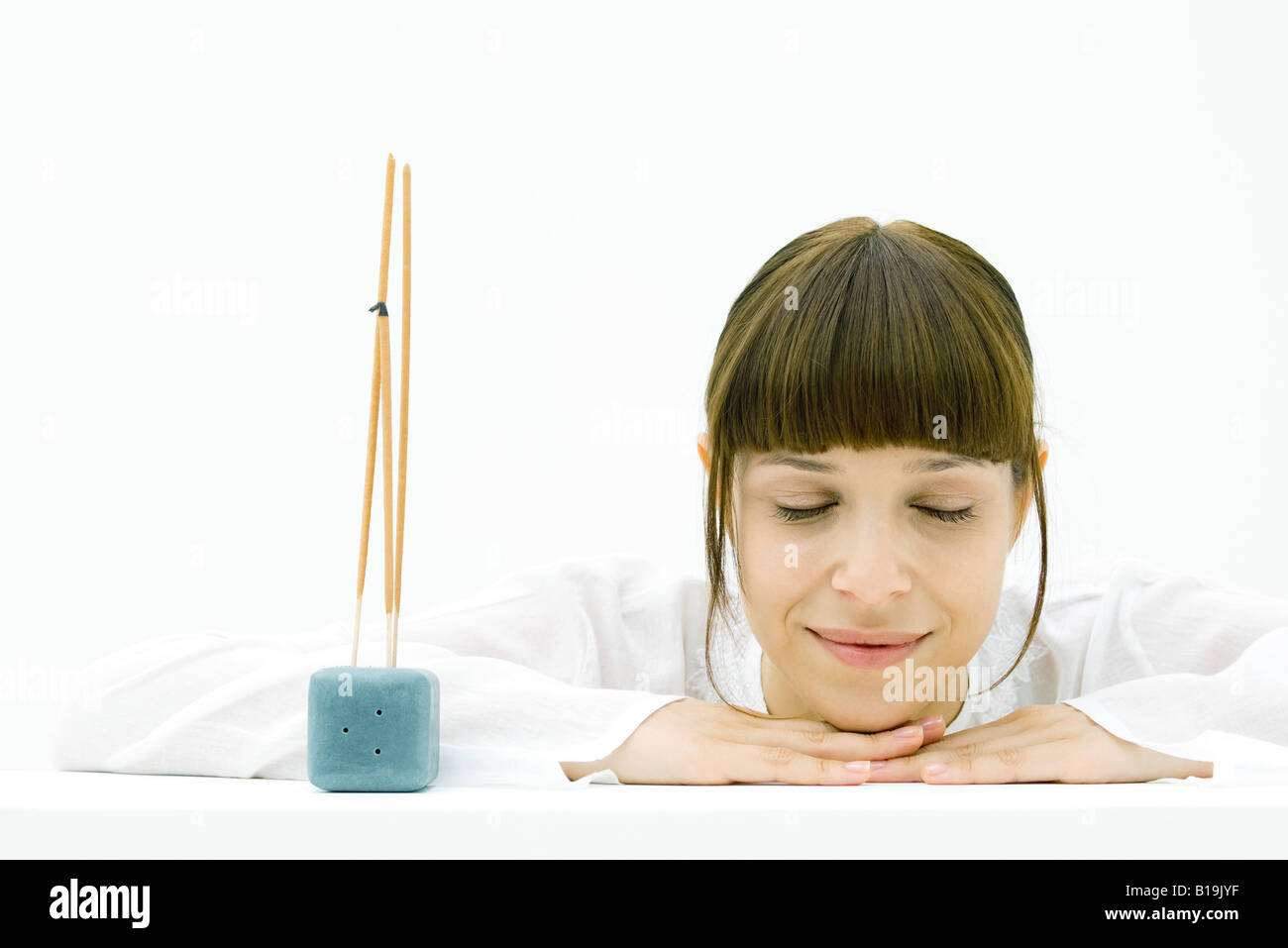 Woman resting head on arms beside incense, eyes closed, smiling Stock Photo
