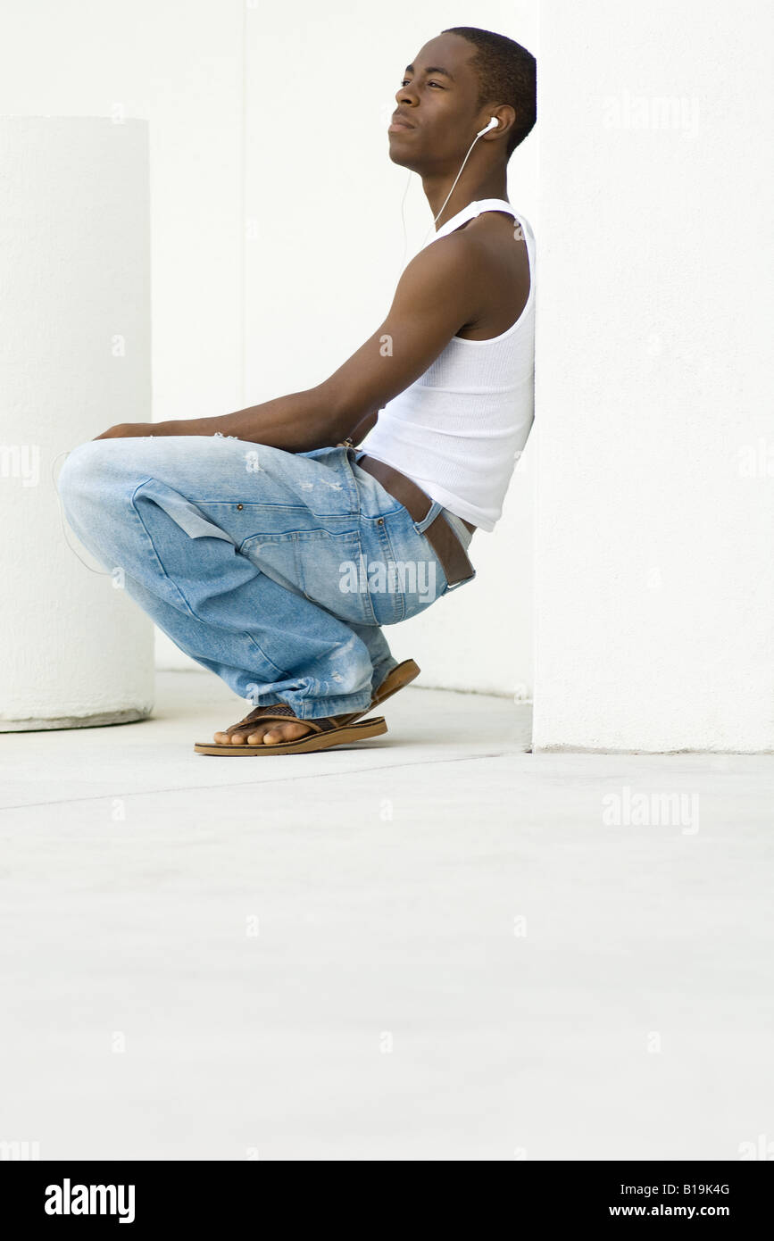 Teen boy crouching listening to earphones side view Stock Photo