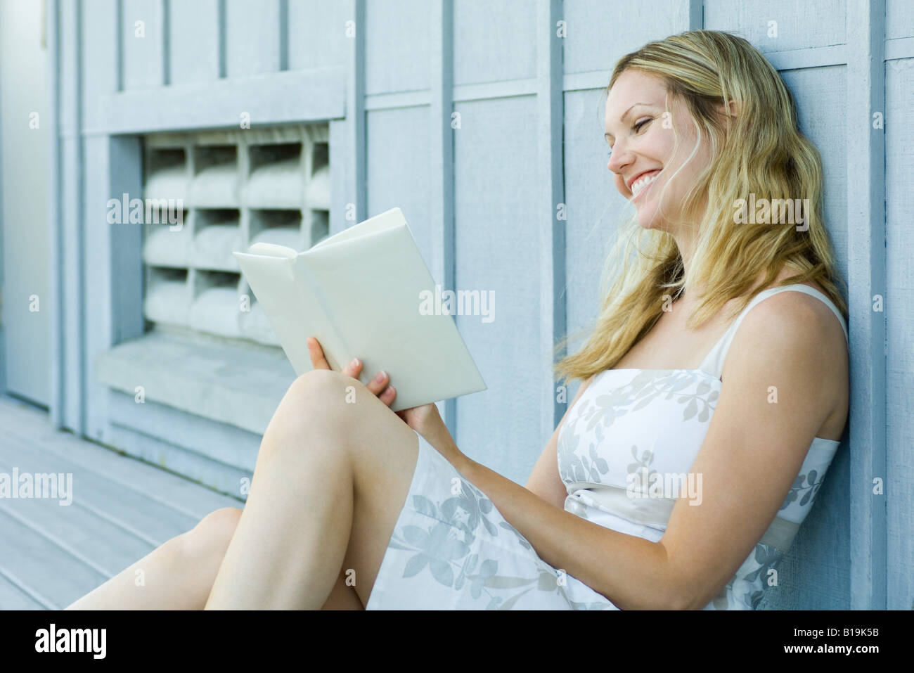 Young woman sitting outdoors, reading book, smiling Stock Photo