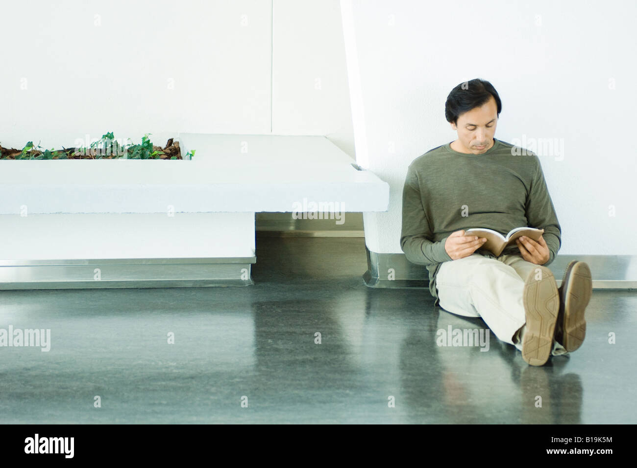 Man sitting on the ground, reading book, full length Stock Photo