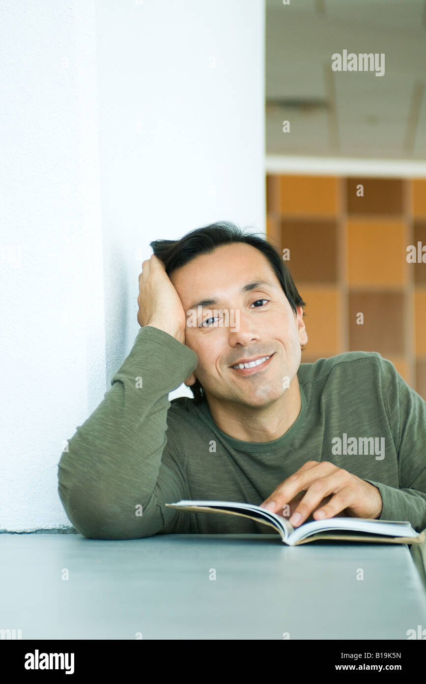 Man sitting with book, holding head, smiling at camera Stock Photo
