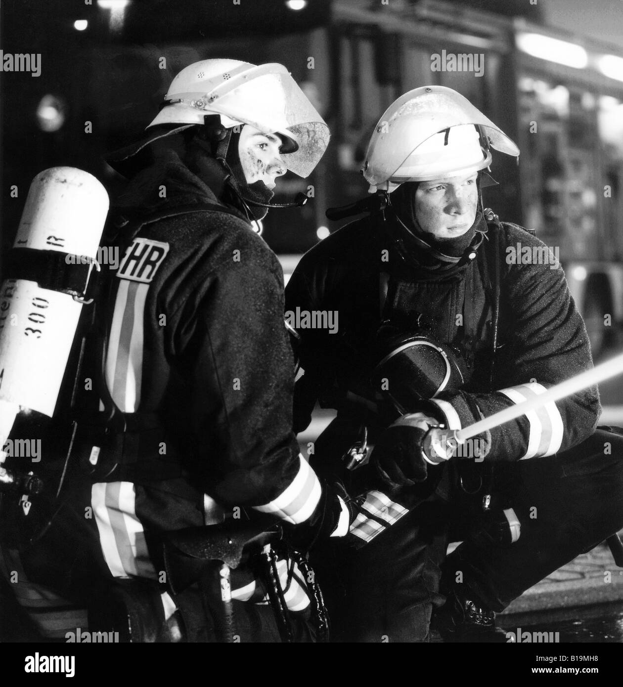 young firefighters with breathing protection and extinguisher in action, at night, black and white, Germany Stock Photo