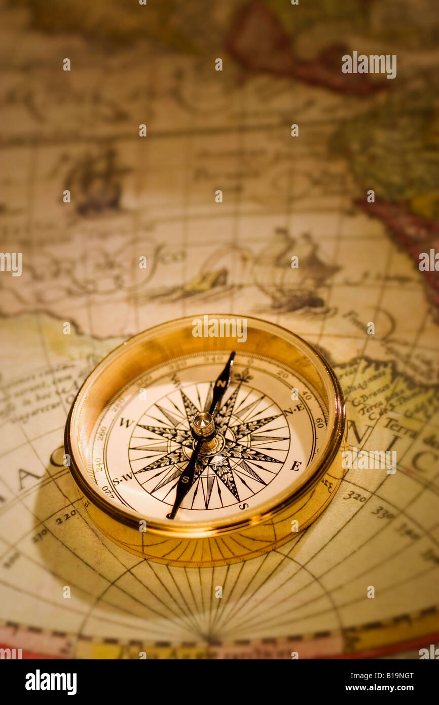 An antique gold compass set upon a sixteenth century map of the world Stock Photo