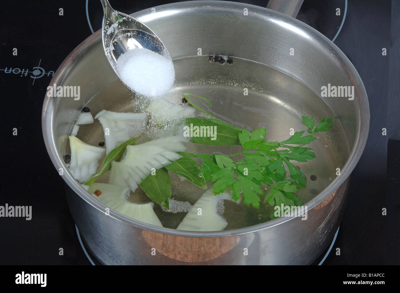 Adding salt to water with bay leaf, peppercorns, parsley, and onion to cook seafood Stock Photo