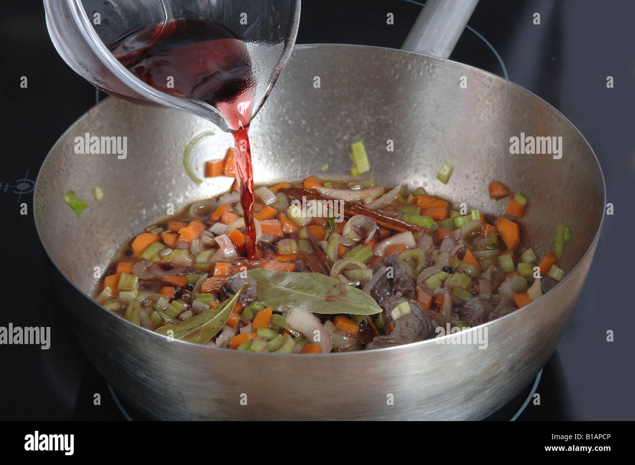 Pouring white wine to vegetables while frying lightly Stock Photo - Alamy
