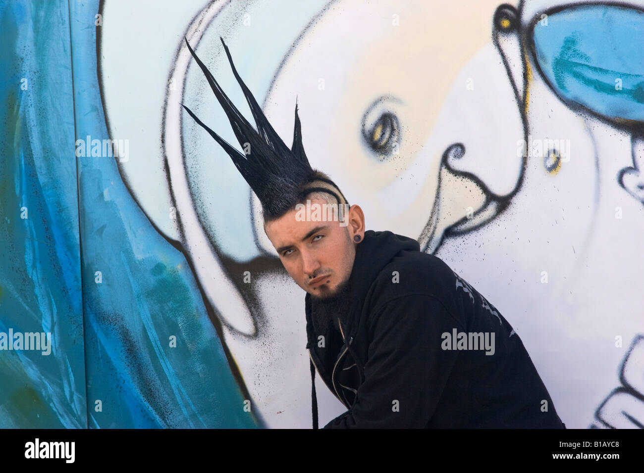 Punk teenager with spikey hairstyle kneeling by street art. Stock Photo