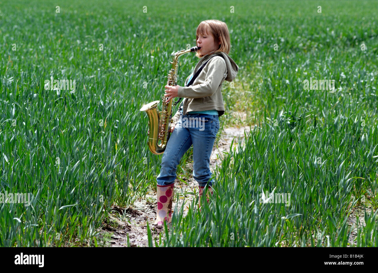Little girl playing the saxophone in a field of crops Walking through the English countryside Stock Photo