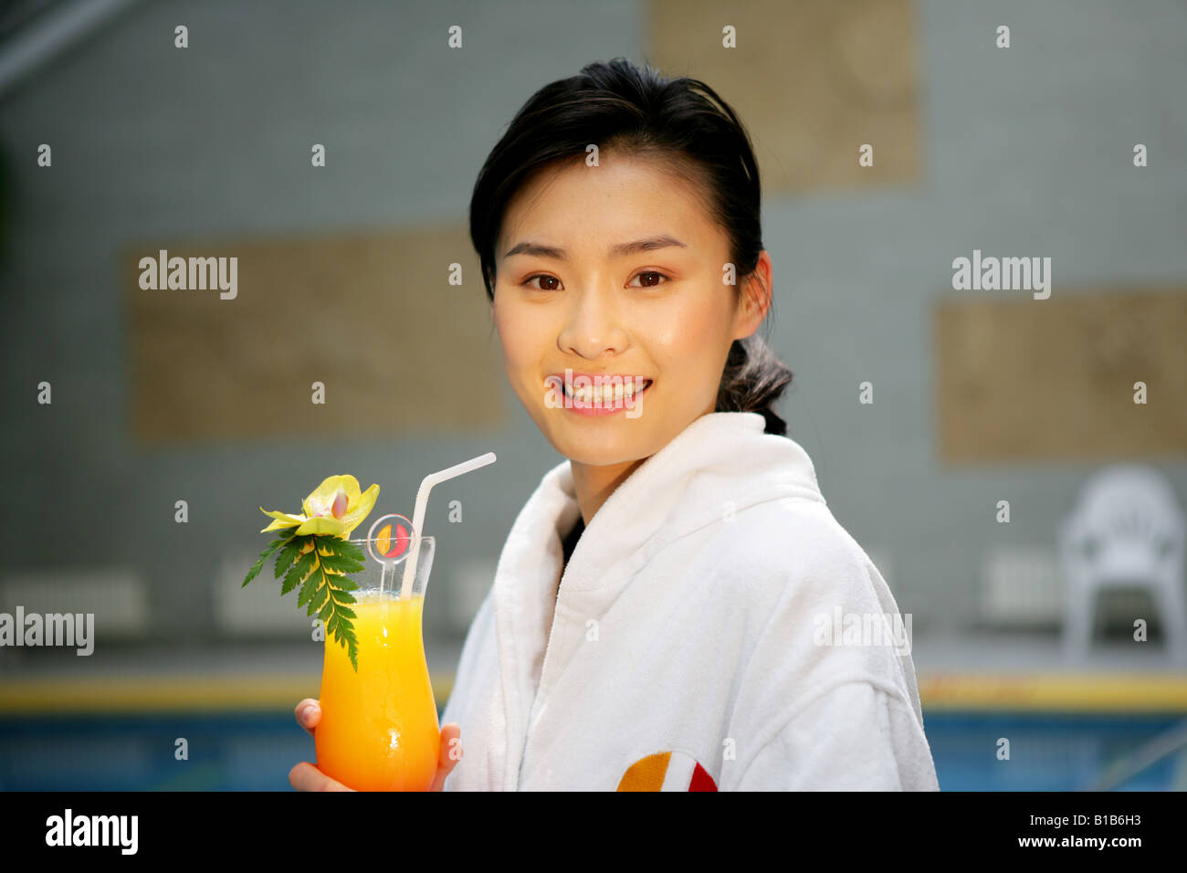 young woman holding juice beside swimming pool in hotel Stock Photo