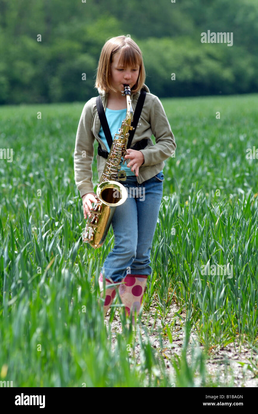 Little girl playing the saxophone in a field of crops Walking through the English countryside Stock Photo