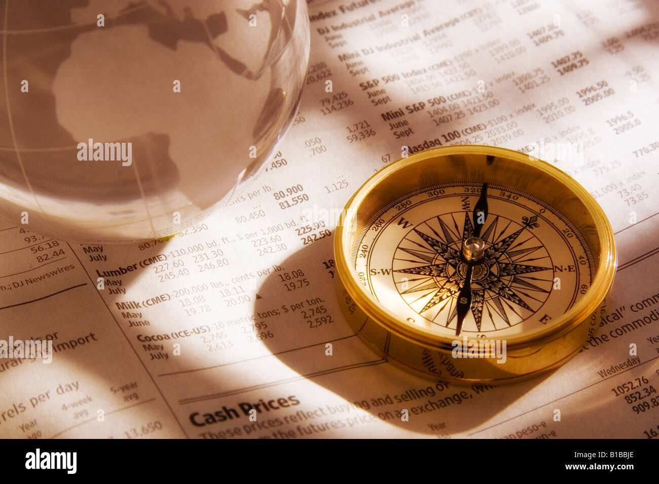 An antique gold compass on the financial page of a newspaper along with a crystal world globe Stock Photo