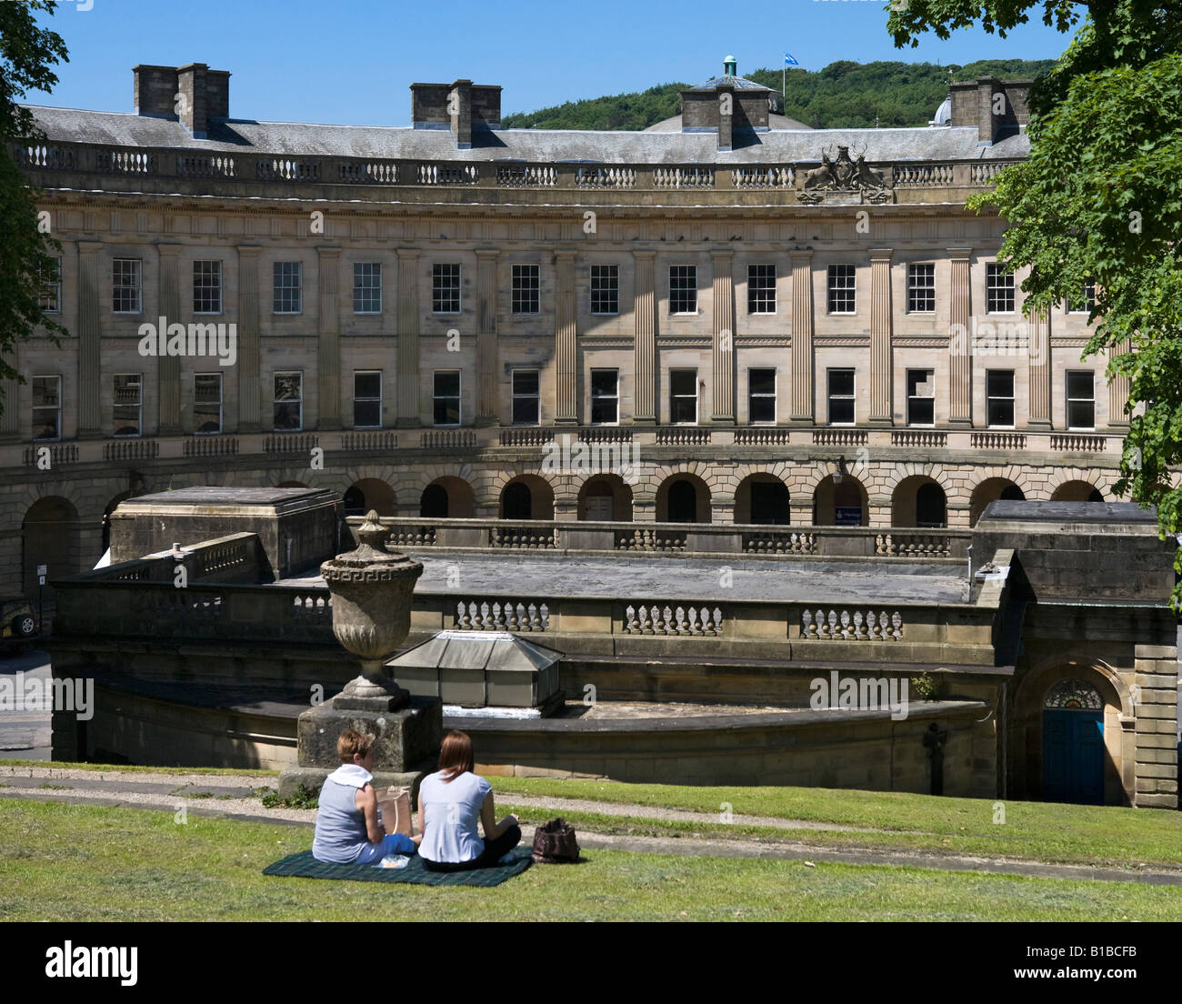 Two women eating picnic lunch overlooking The Crescent & Pump Room, The Slopes, Buxton, Peak District, Derbyshire, England Stock Photo