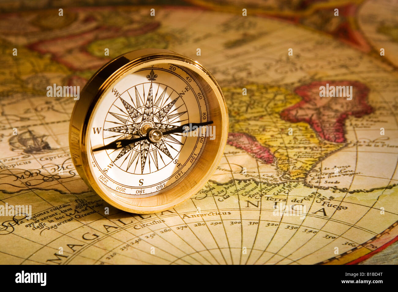 An antique gold compass set upon a sixteenth century map of the world Stock Photo