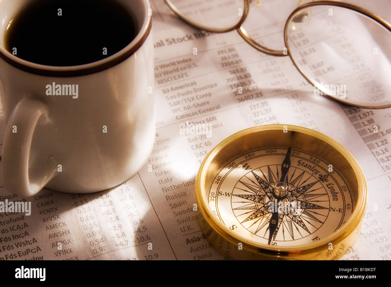 An antique gold compass on the financial page of a newspaper along with a coffee mug and reading glasses Stock Photo