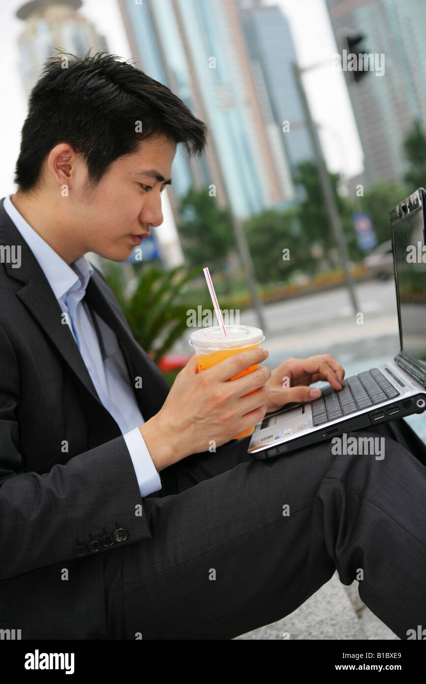 one businessman drinking orange juice while using a laptop outside office buildings in Pudong