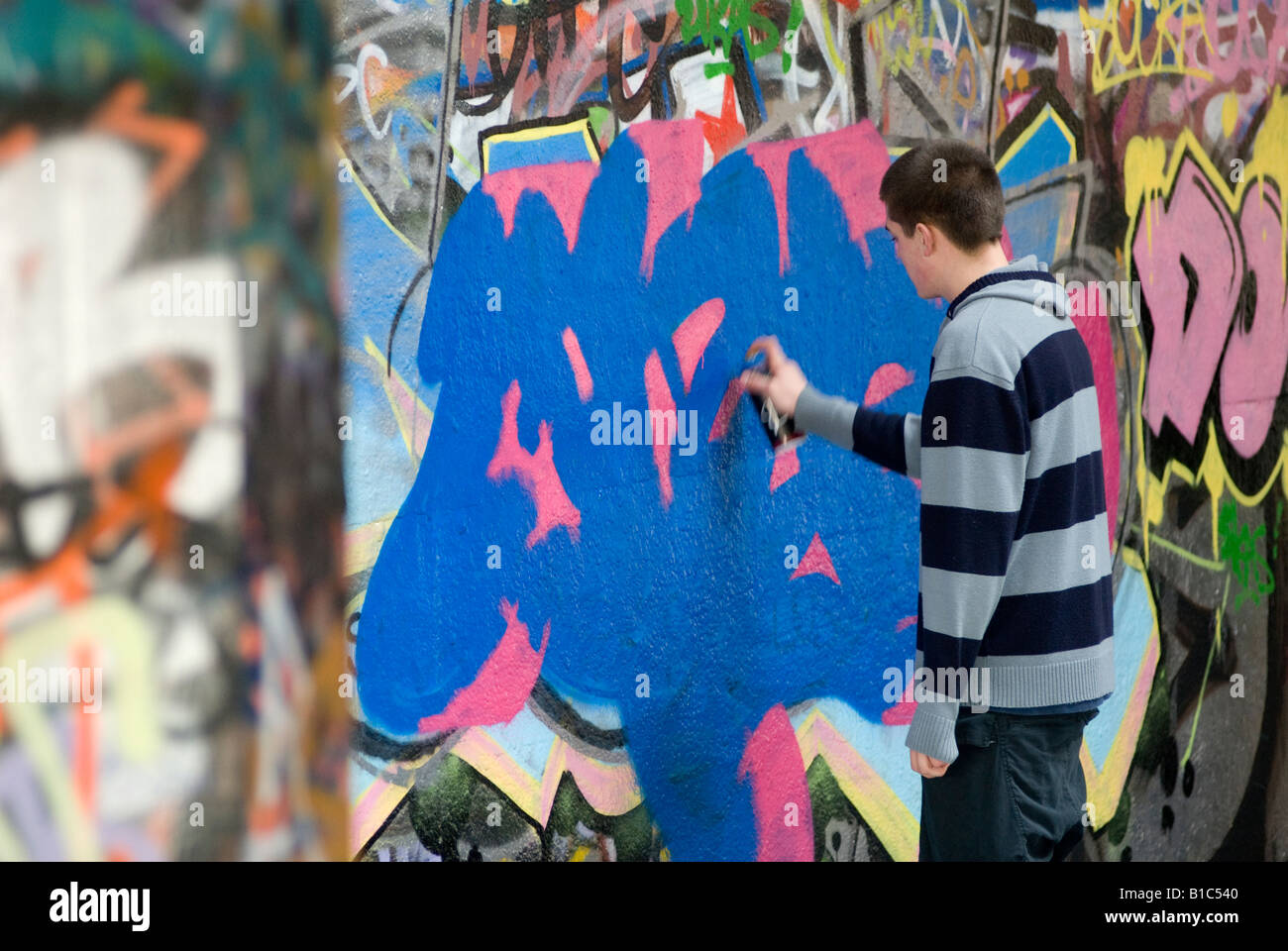 youth using a can of spray paint to graffiti on a wall in the centre of ...