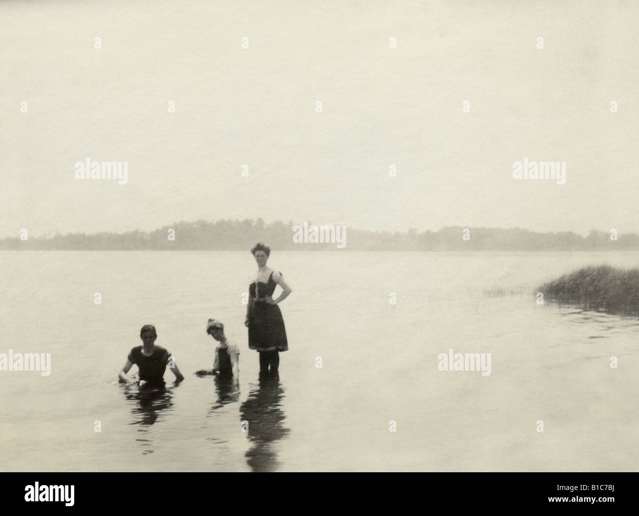 Antique photograph, circa 1890s, of two women and 1 man dressed in Victorian-era bathing suits swimming in a New England lake. Stock Photo
