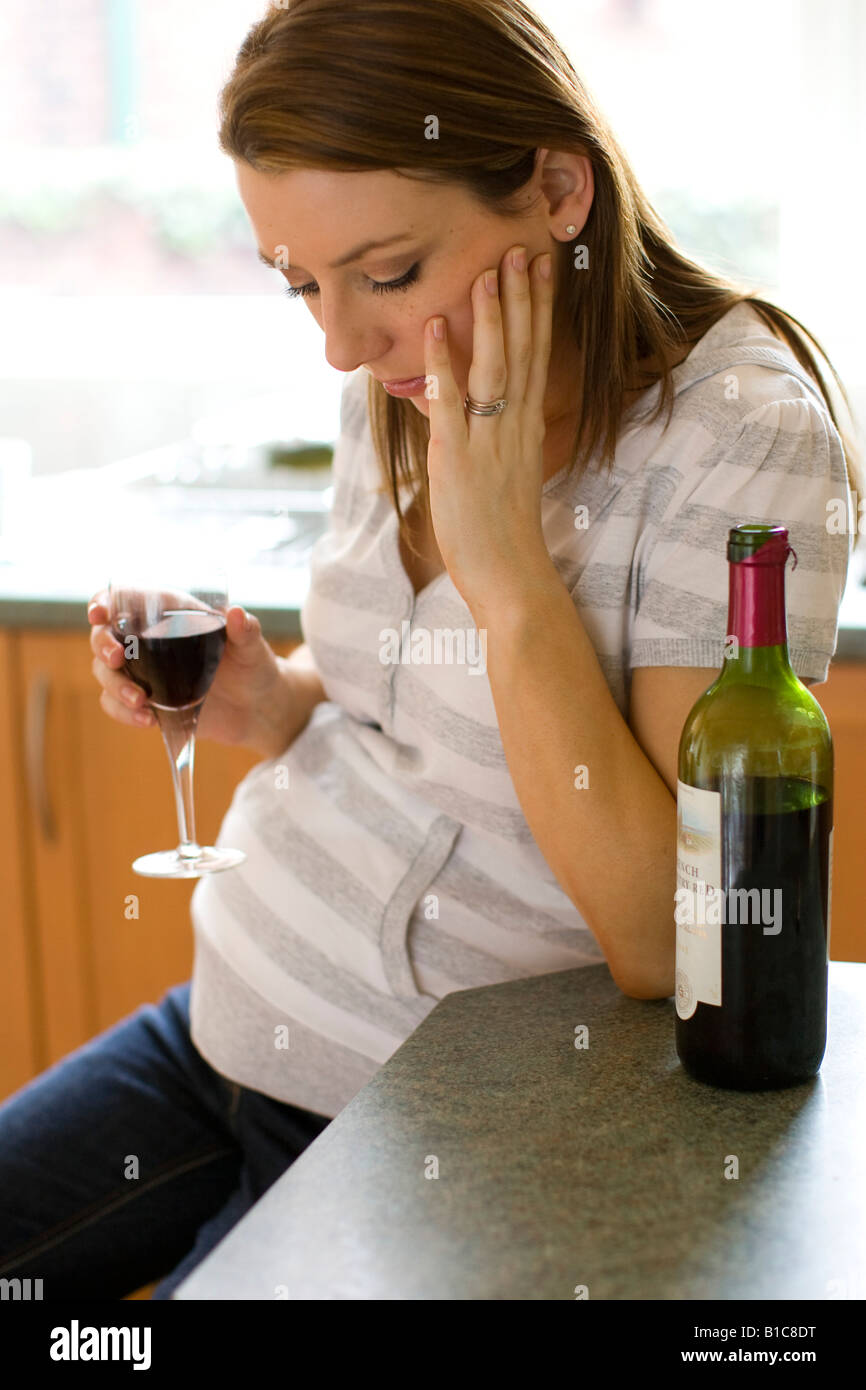 Worried looking pregnant woman drinking wine Stock Photo