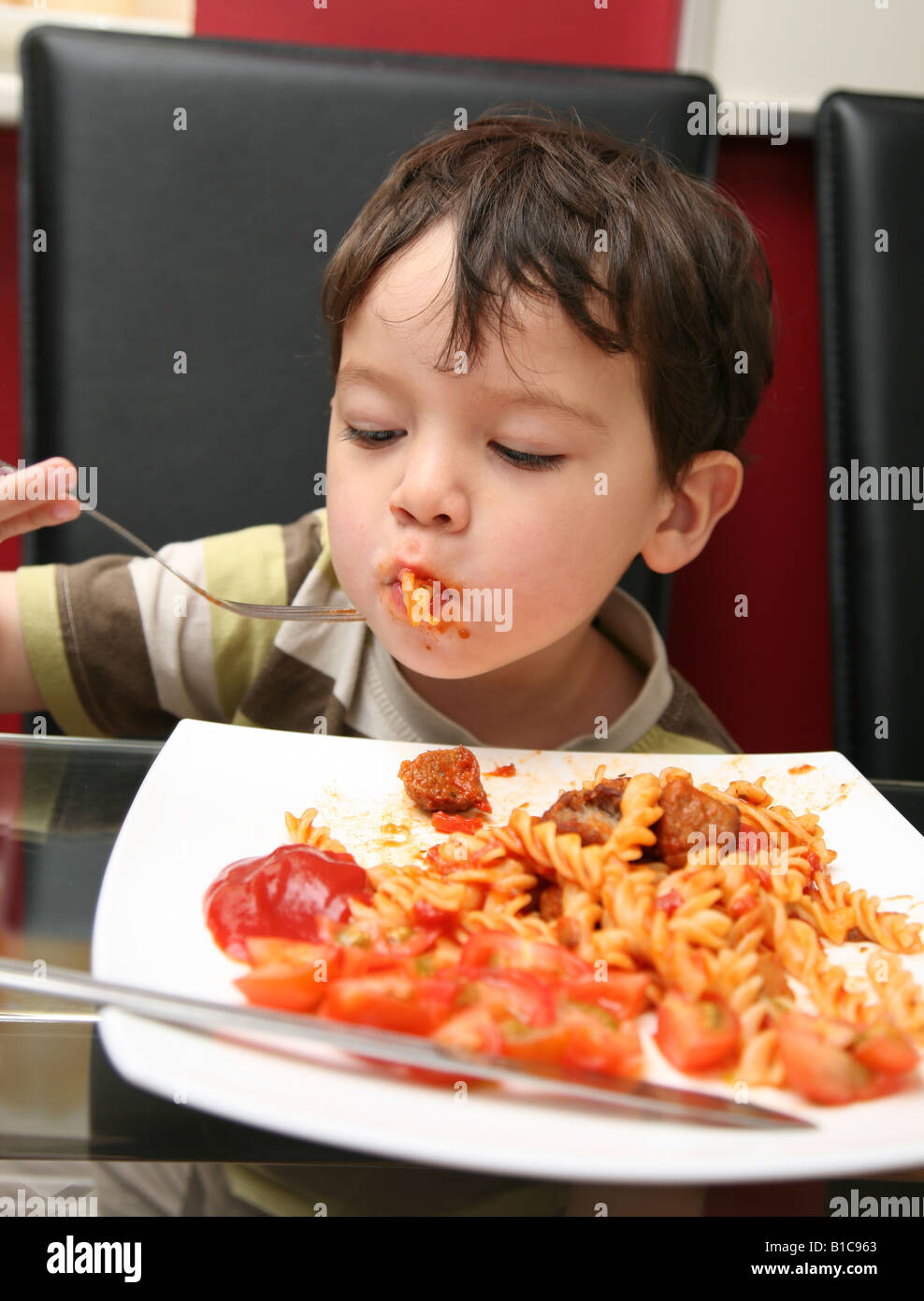 2 year old boy sitting at the dinner table eating dinner Stock Photo