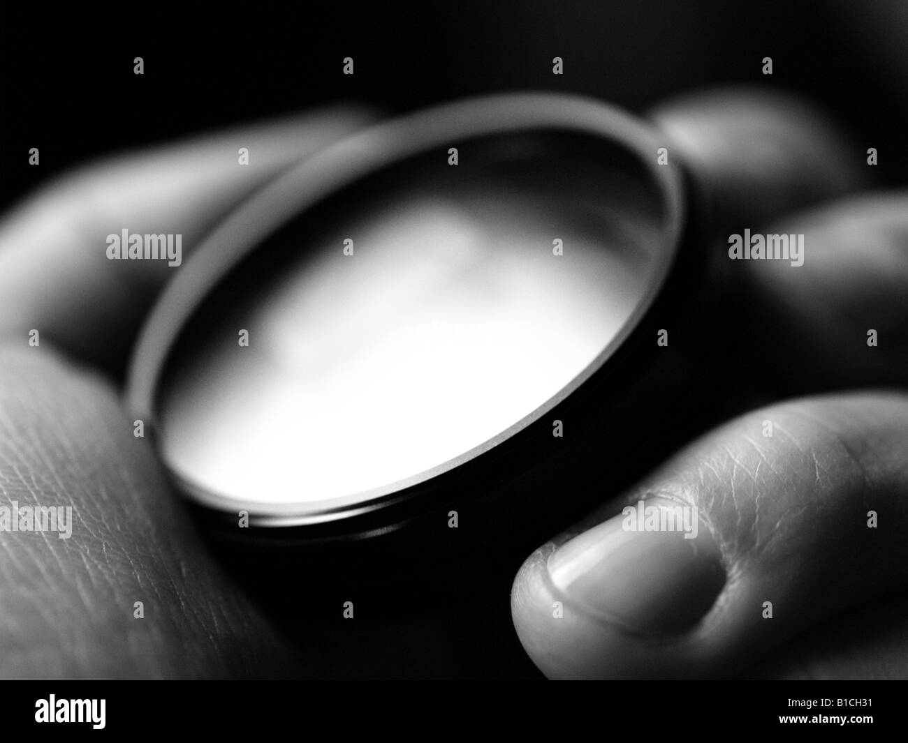 Black and white close-up of hand holding a UV filter lens. Stock Photo