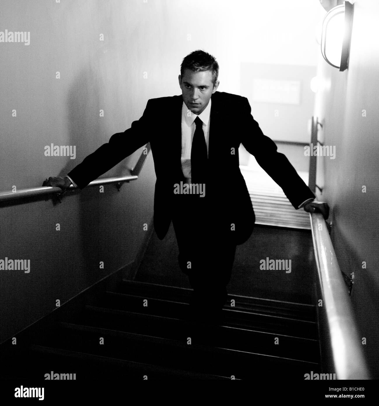 man in a dark suit ascends a shadowy stairwell Stock Photo