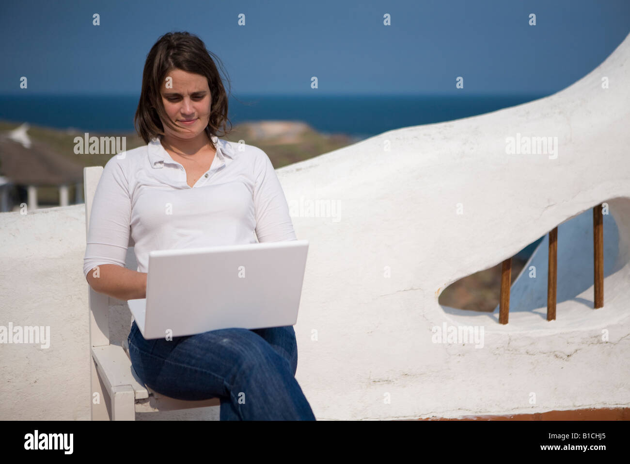 Young woman writting on her macbook laptop in a mediterranean terrace in Casapueblo Punta del Este Uruguay Stock Photo
