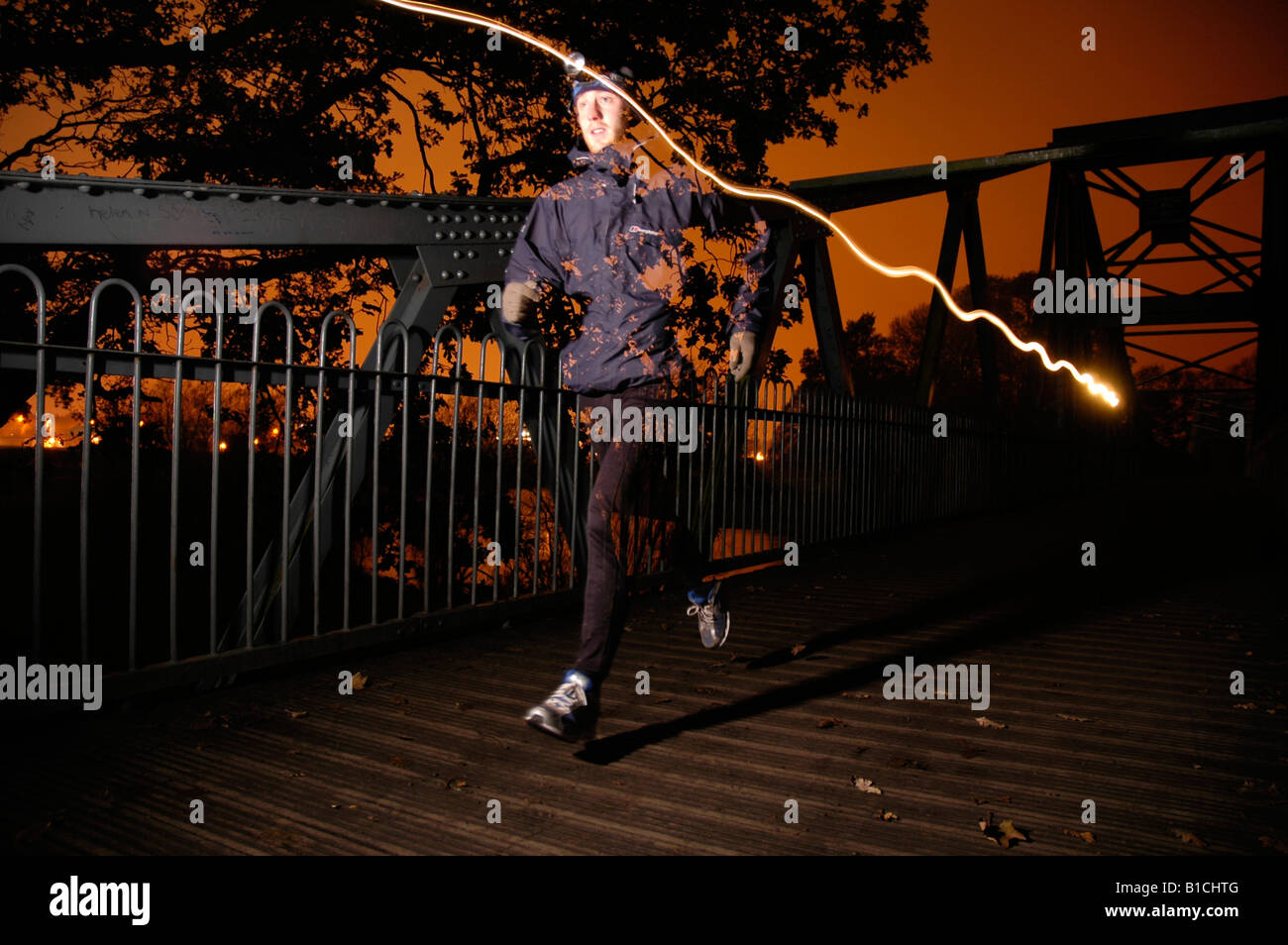 Runner on a bridge at night sunset sky and line from head torch Stock Photo