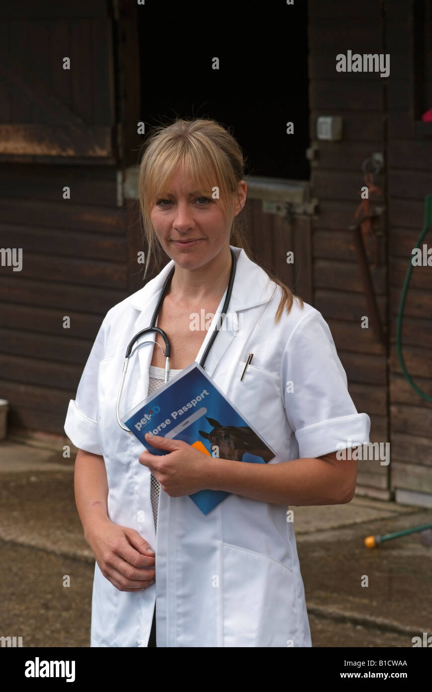 Female vet standing in a stable yard wearing a white coat and
