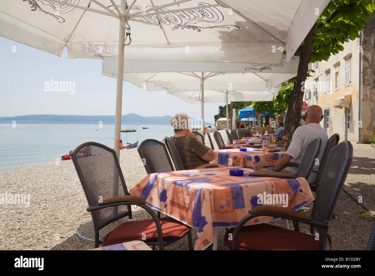 Moscenicka Draga Istria Croatia Street cafe with people sitting at tables with umbrellas outside on seafront by beach Stock Photo