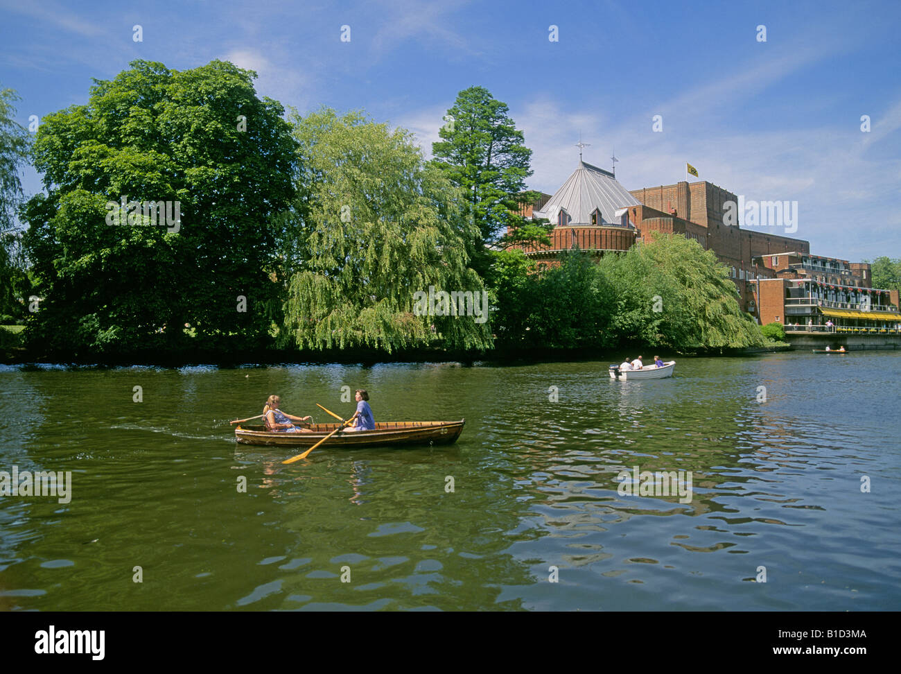Visitors row a small skiff on the Avon River in Stratford Upon Avon in front of the Royal Shakespeare Theater Stock Photo