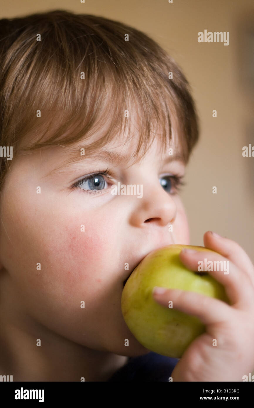 Portait of a young boy with blonde hair bitting into an apple Stock Photo