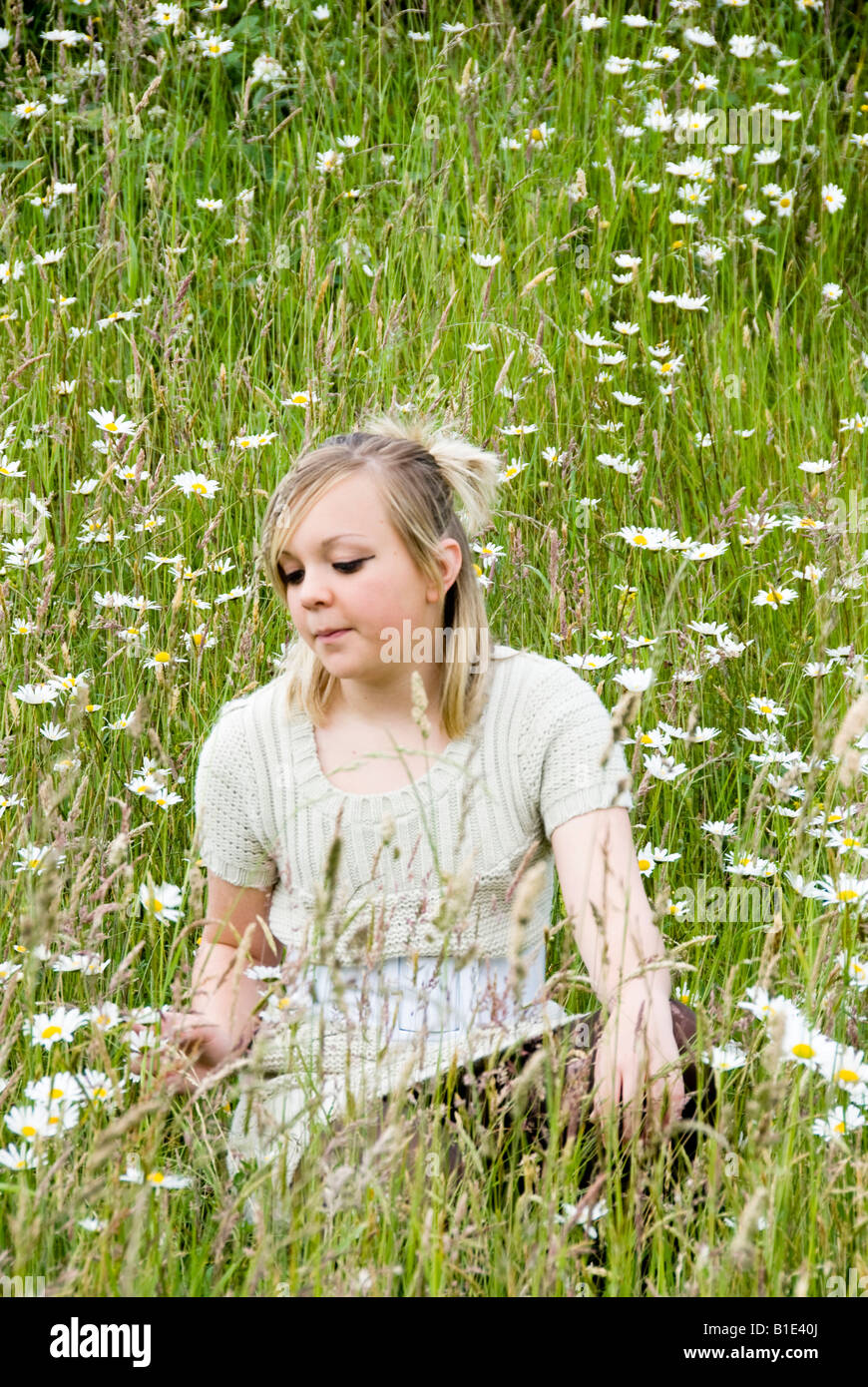 blonde female teenager sitting amongst wild flowers Stock Photo
