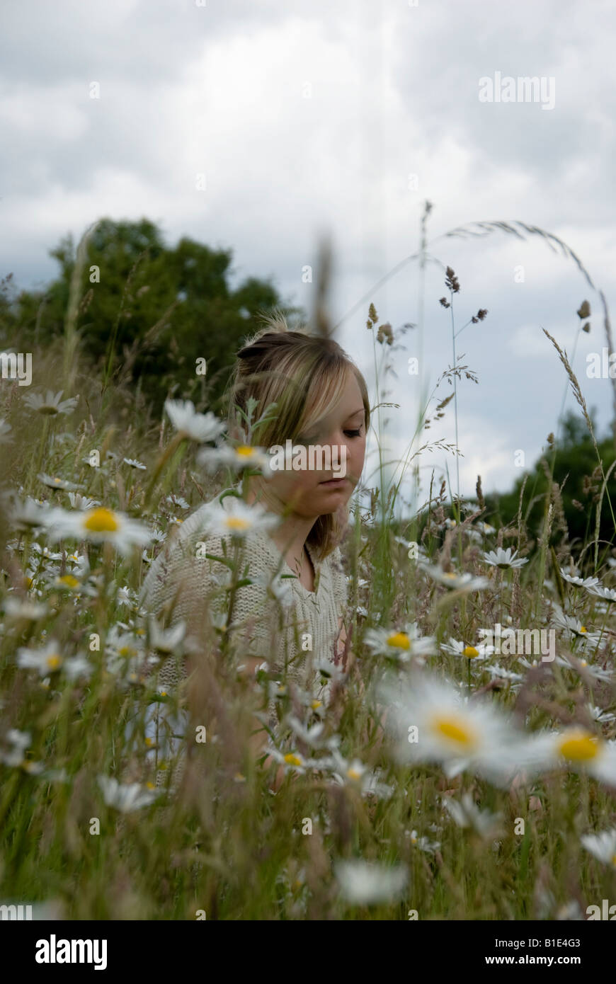 blonde female teenager sitting amongst wild flowers Stock Photo