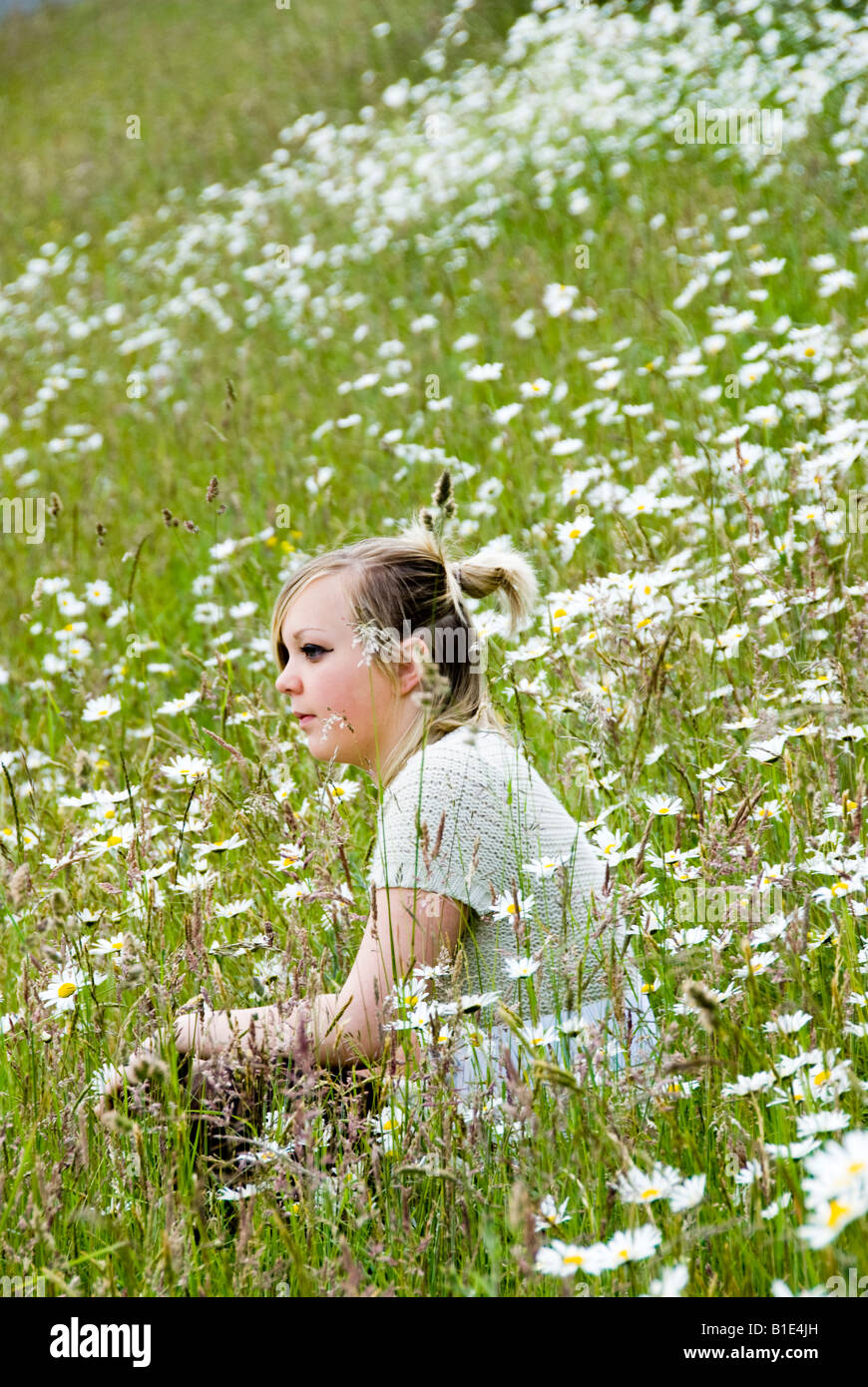 blonde female teenager sitting amongst wild flowers Stock Photo