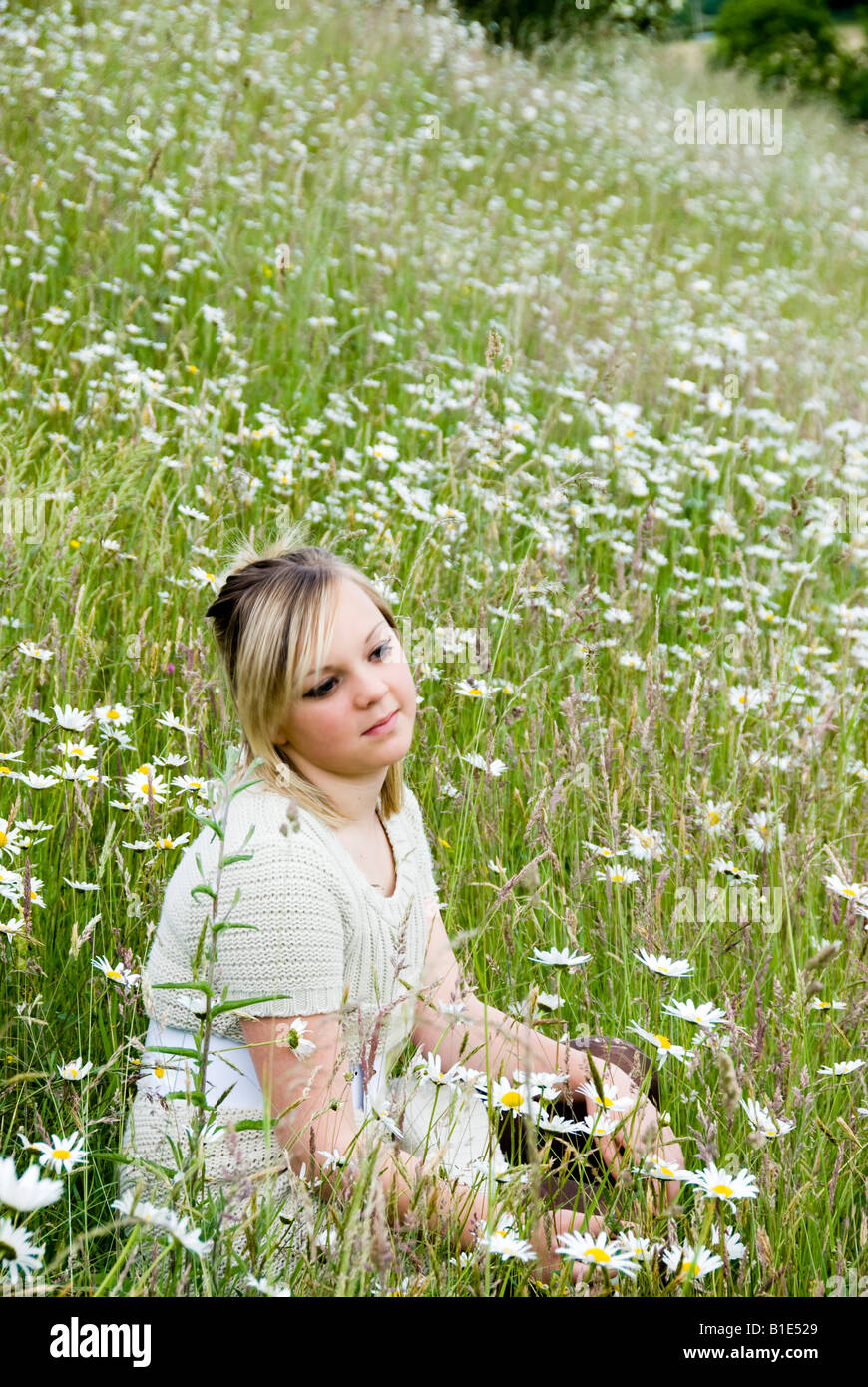 blonde female teenager sitting amongst wild flowers Stock Photo