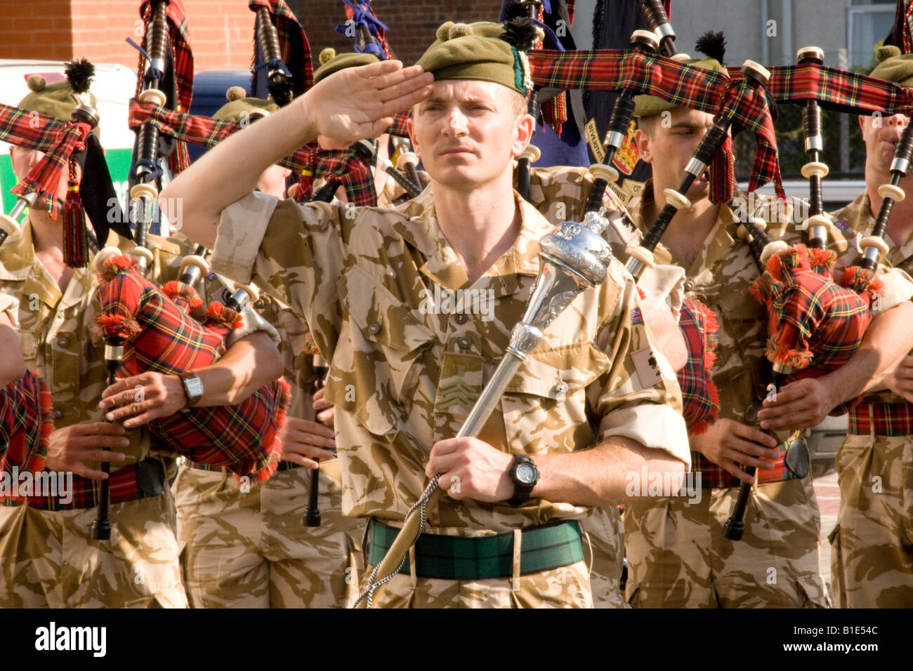 Scottish soldiers pipe major saluting before beating the retreat with bagpipers in military uniform behind desert fatigues Stock Photo