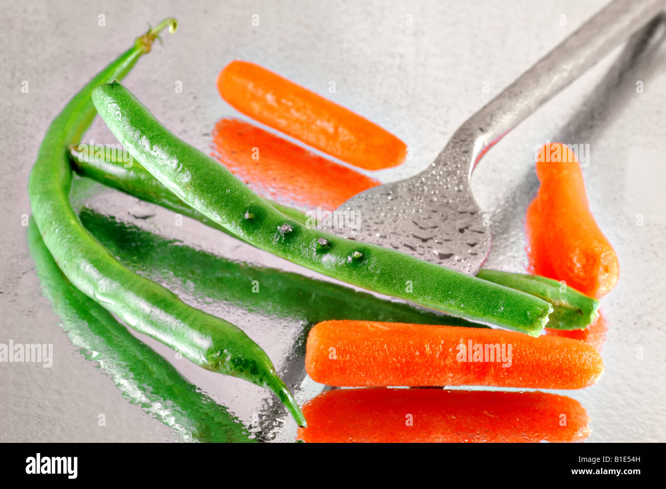 Fresh green beans and baby carrots pierced with a fork on a reflective