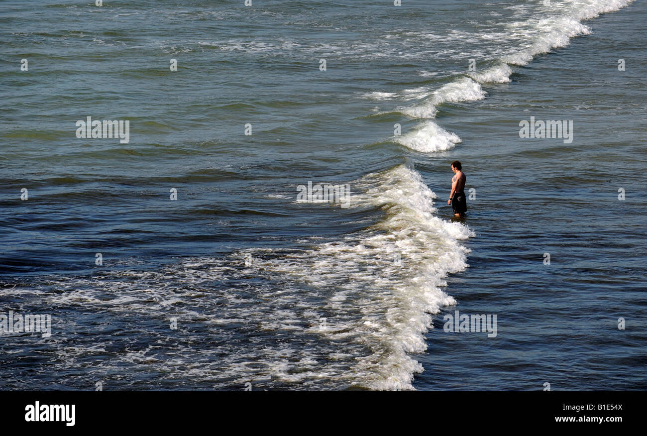MAN STANDING ALONE IN WAVES LOOKING OUT TO SEA RE ALONE LONELY DEPRESSION THOUGHTFUL HOLIDAY HOLIDAYS BEACH COAST COASTAL ETC UK Stock Photo