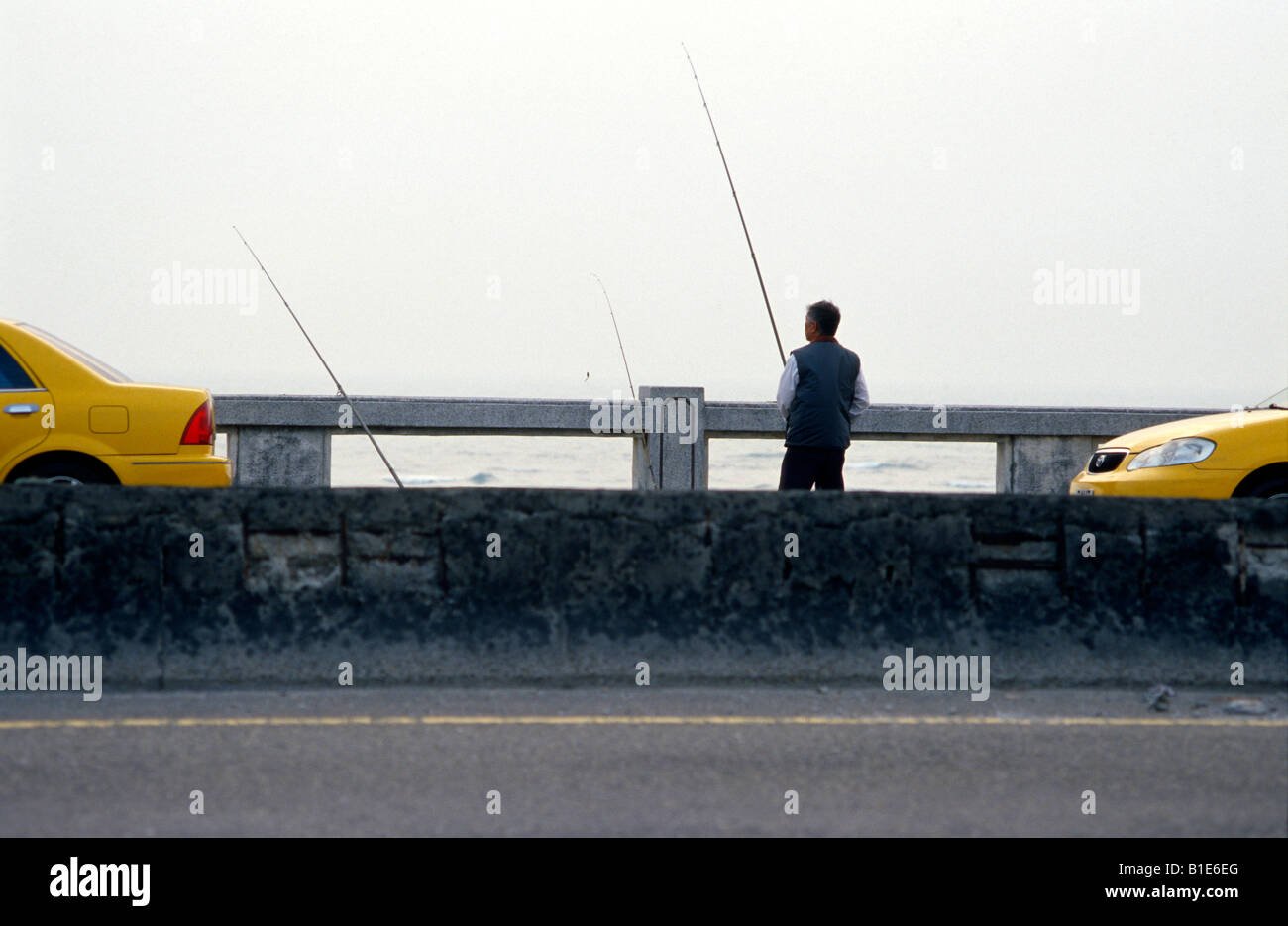 A taxi driver in Taiwan fishes off a bridge in winter on Golden Coast Highway. Kaohsiung County, Taiwan.. Stock Photo