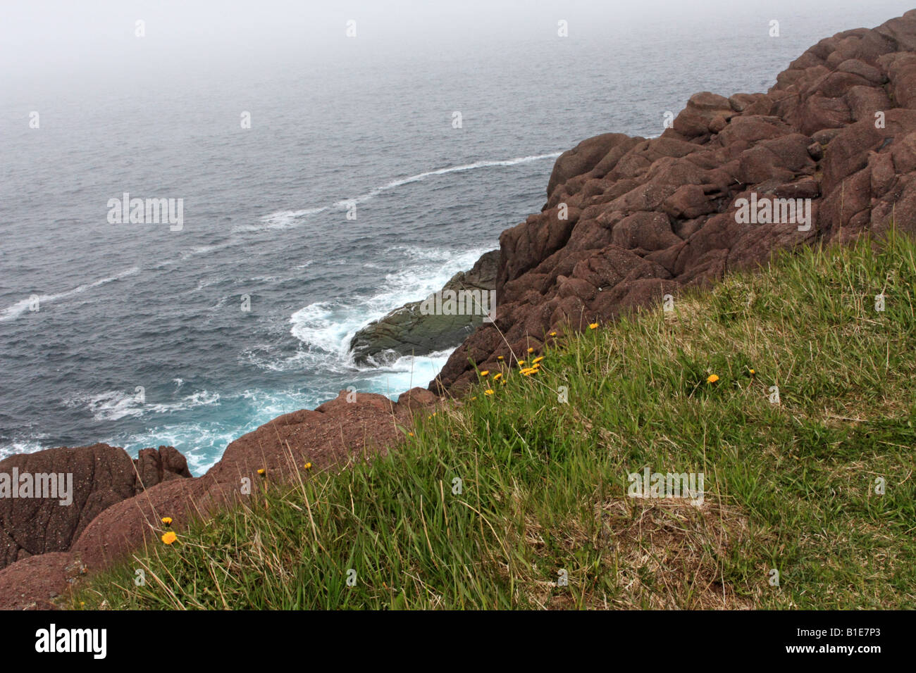 Rocky cliff of Cape Spear over foggy and steel grey Atlantic Ocean in Newfoundland Stock Photo