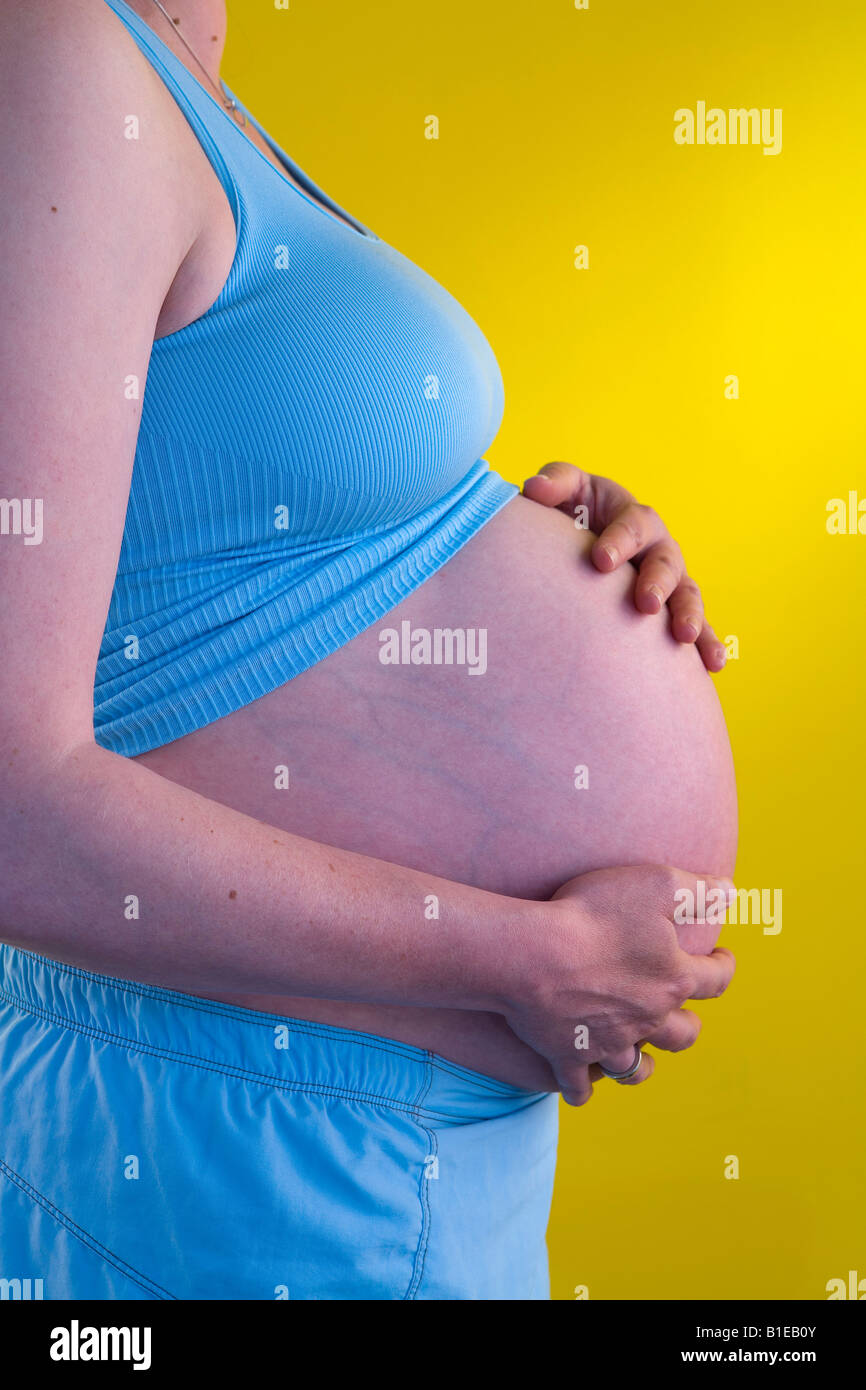 Side view of pregnant woman with hands on her stomach and wearing a