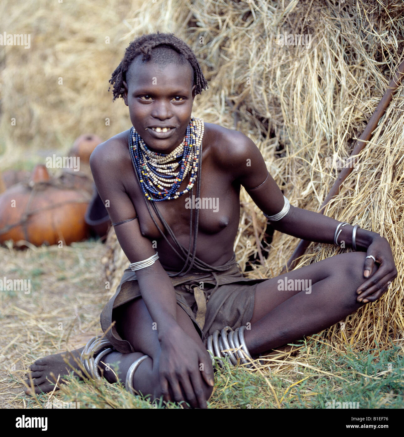 An attractive Dassanech girl sits outside her home in the Omo Delta. In the background are her gourds used for water and milk. Stock Photo
