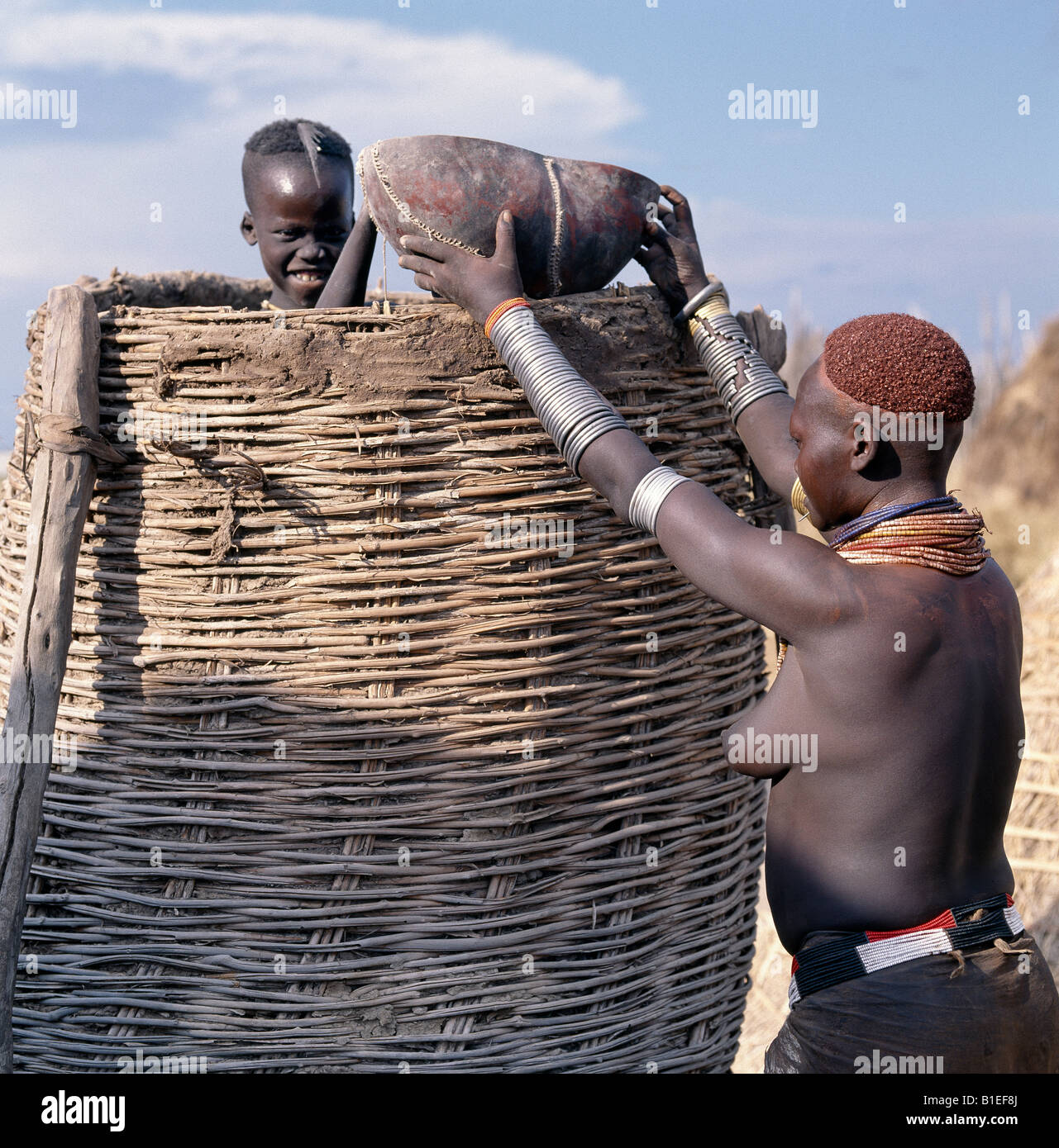 A Karo woman is helped by a member of her family to take grain out of a traditional granary in the village of Duss. Stock Photo