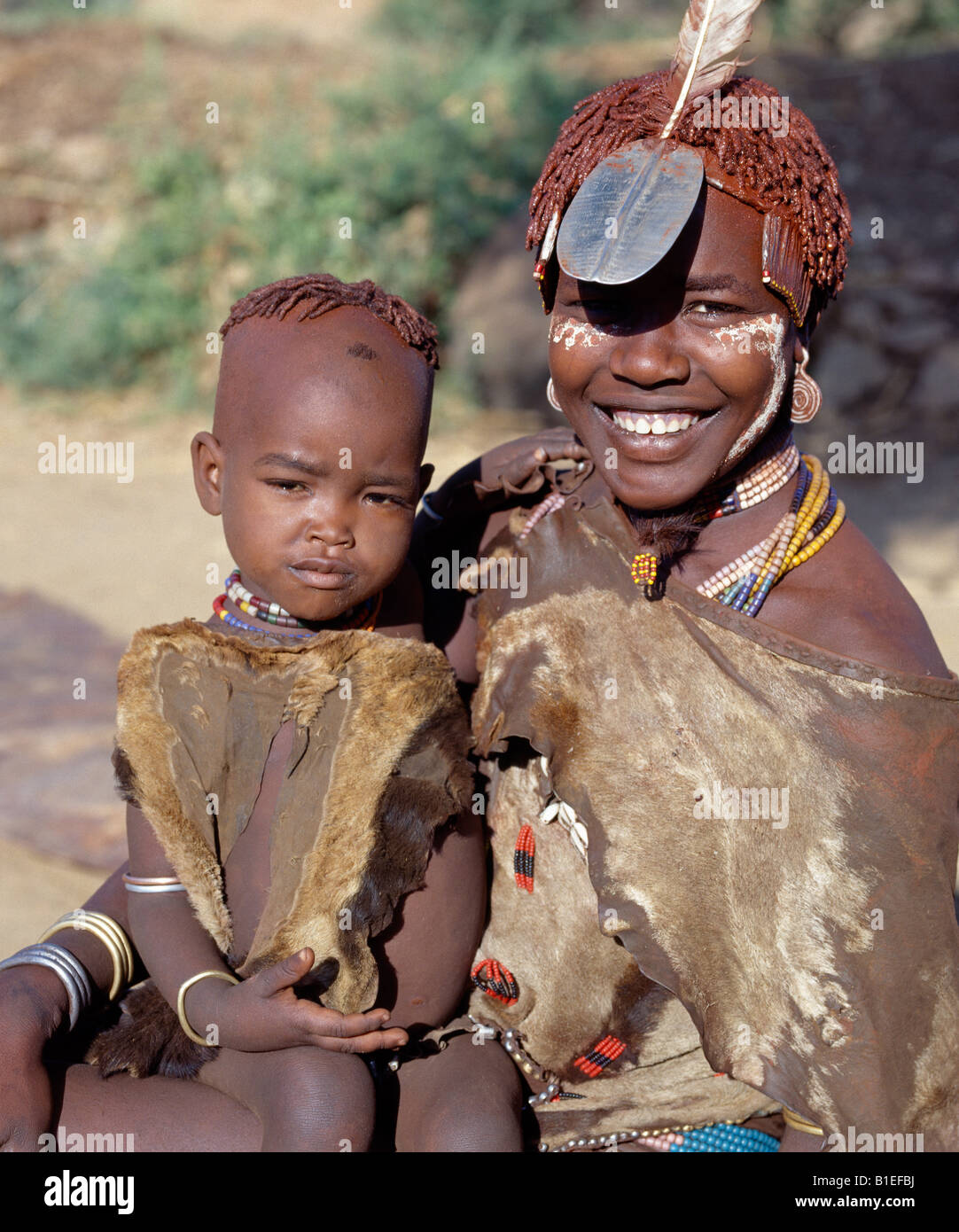 A happy Hamar girl with her young sister on her lap.The Hamar of Southwest Ethiopia are semi-nomadic pastoralists. Stock Photo