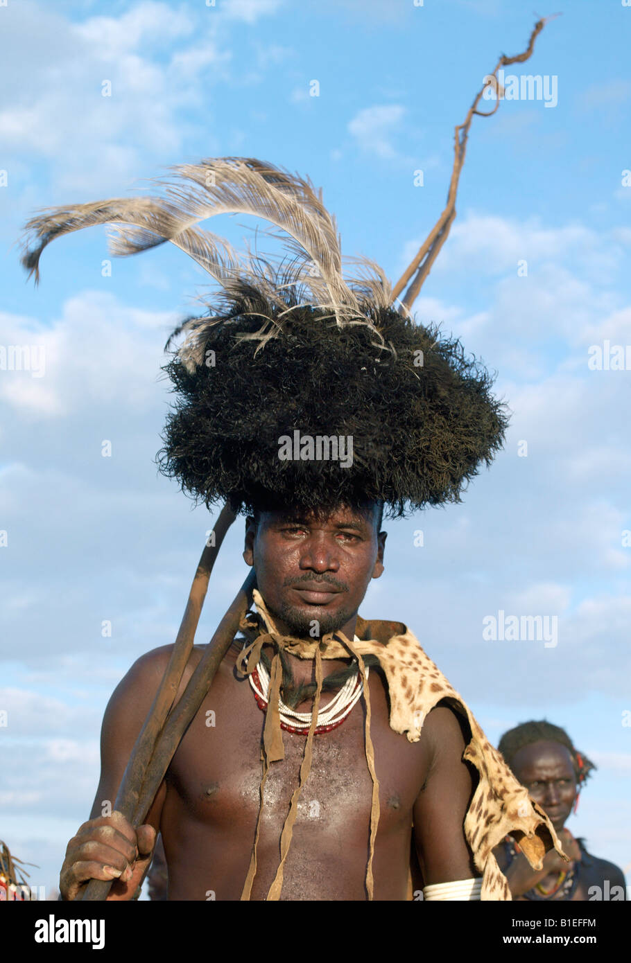 In the early morning, a Dassanech man puts on his serval cat skin cape and ostrich-feather headdress to participate. Stock Photo